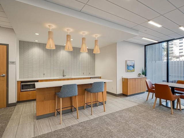 kitchen with a kitchen breakfast bar, a drop ceiling, light tile patterned floors, and sink