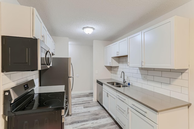 kitchen with sink, appliances with stainless steel finishes, light hardwood / wood-style flooring, and white cabinets