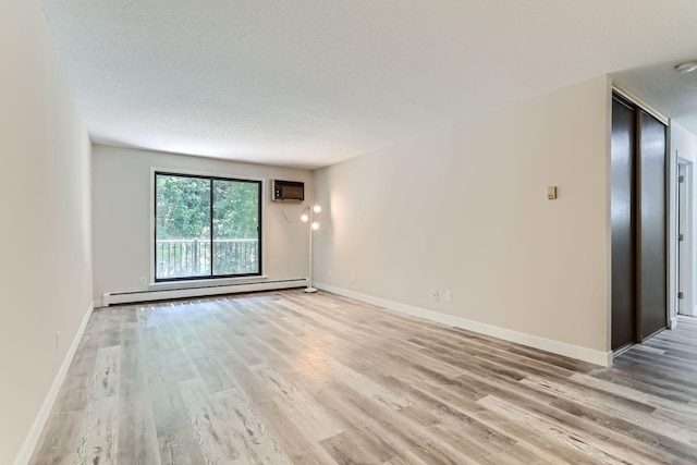 empty room with light hardwood / wood-style floors, a textured ceiling, baseboard heating, and an AC wall unit