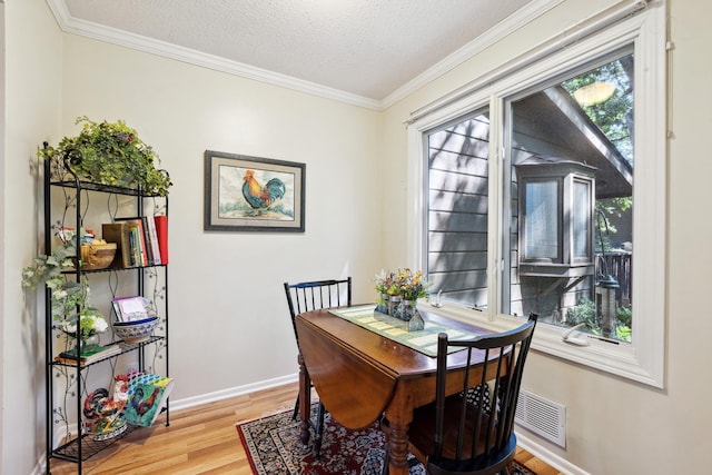 dining space featuring light hardwood / wood-style floors, a textured ceiling, and ornamental molding