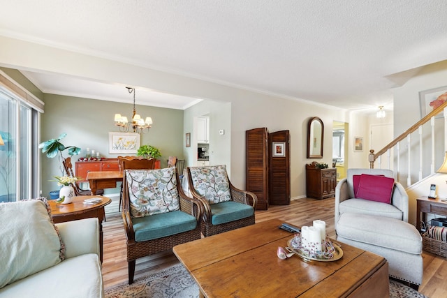 living room featuring crown molding, a notable chandelier, a textured ceiling, and light wood-type flooring