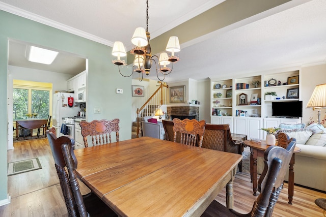 dining room with ornamental molding, a chandelier, light hardwood / wood-style flooring, and a brick fireplace