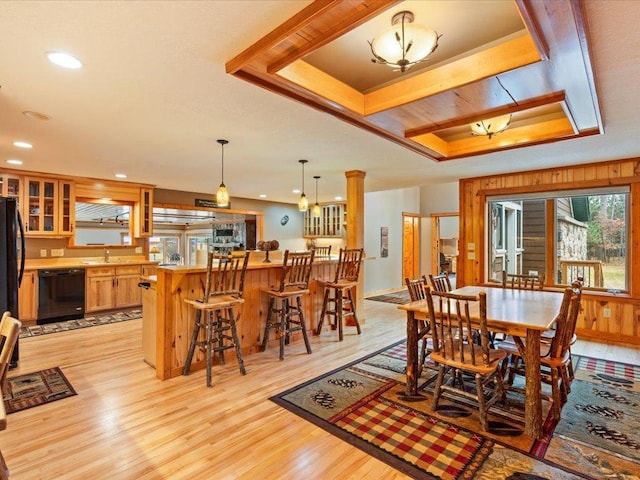 dining space with a tray ceiling, wood walls, sink, and light wood-type flooring