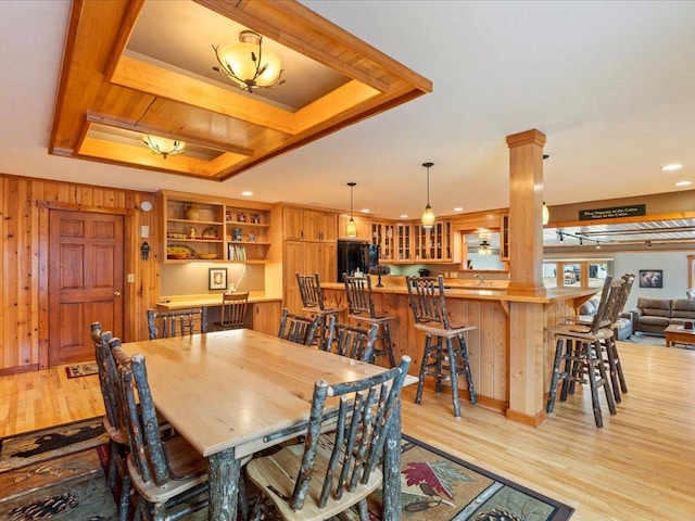 dining area featuring a tray ceiling, ornate columns, wooden walls, and light wood-type flooring