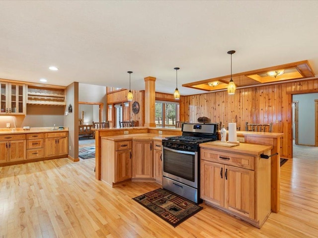 kitchen with stainless steel range with gas cooktop, kitchen peninsula, light wood-type flooring, and decorative light fixtures