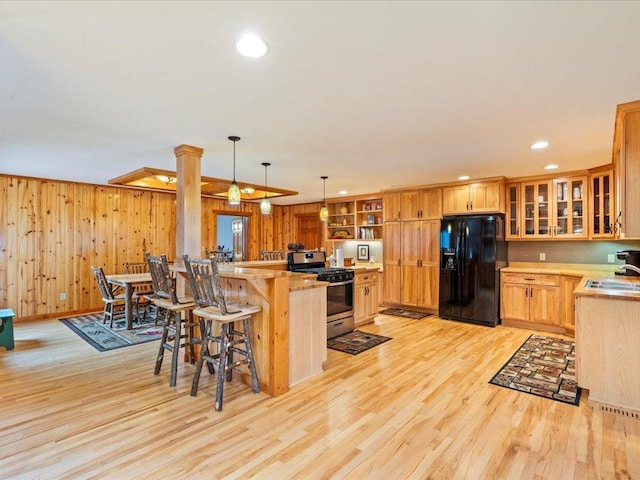 kitchen with hanging light fixtures, black fridge, stainless steel range with gas cooktop, kitchen peninsula, and light wood-type flooring