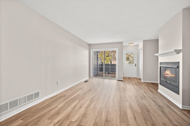 unfurnished living room with light wood-type flooring and a textured ceiling