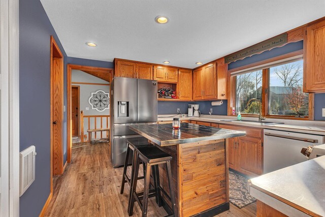 kitchen featuring stainless steel appliances, sink, a kitchen breakfast bar, light hardwood / wood-style flooring, and a kitchen island