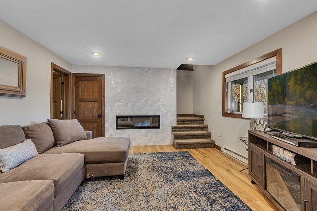 living room with a baseboard heating unit, light hardwood / wood-style flooring, and a large fireplace