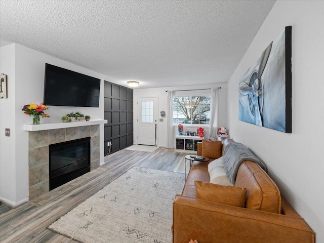 living room with a tiled fireplace, light hardwood / wood-style floors, and a textured ceiling