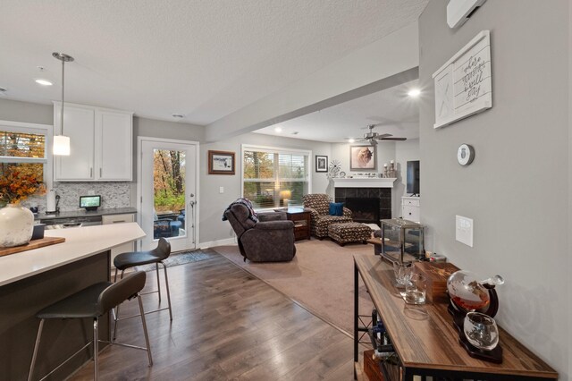 living room with ceiling fan, a textured ceiling, a tile fireplace, and dark hardwood / wood-style floors