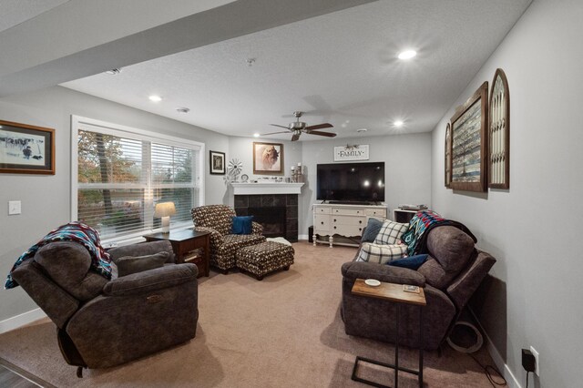 carpeted living room with a tiled fireplace, a textured ceiling, and ceiling fan