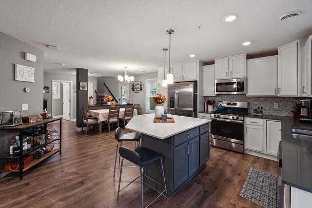 kitchen with appliances with stainless steel finishes, hanging light fixtures, dark hardwood / wood-style floors, and white cabinetry