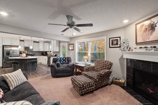 living room featuring dark carpet, a textured ceiling, a tile fireplace, and ceiling fan