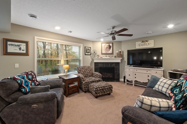 living room with a textured ceiling, a tiled fireplace, light colored carpet, and ceiling fan