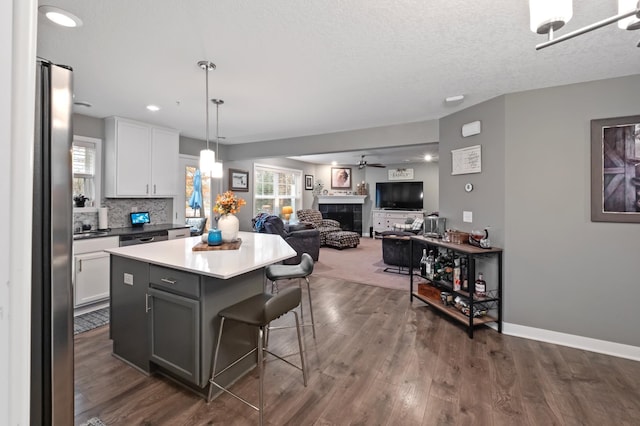 kitchen with a kitchen island, dark wood-type flooring, a tile fireplace, a kitchen bar, and white cabinetry