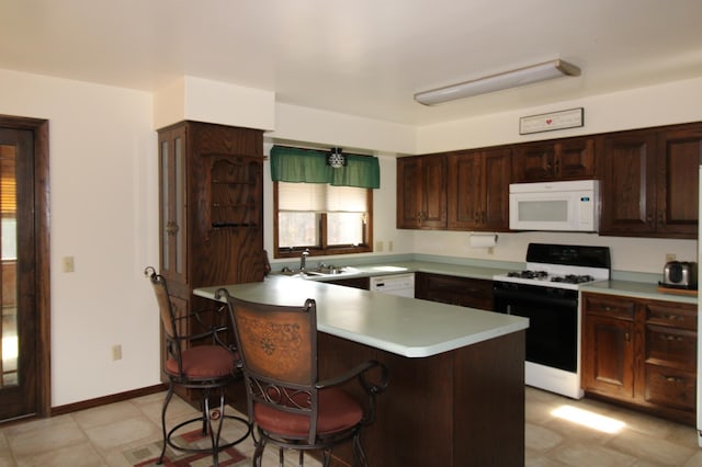 kitchen featuring kitchen peninsula, sink, white appliances, and a breakfast bar area