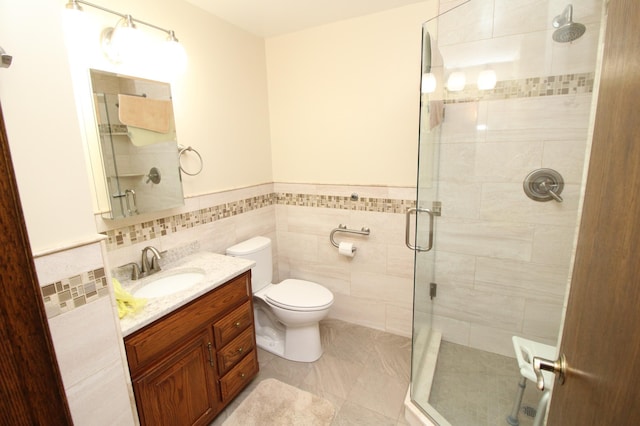 bathroom featuring a shower with door, vanity, toilet, and tile walls