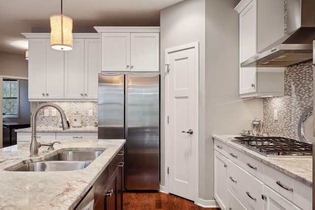 kitchen with wall chimney range hood, sink, decorative light fixtures, white cabinetry, and appliances with stainless steel finishes