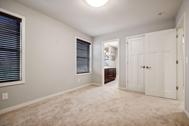 unfurnished bedroom featuring light carpet, a closet, a textured ceiling, and ensuite bath