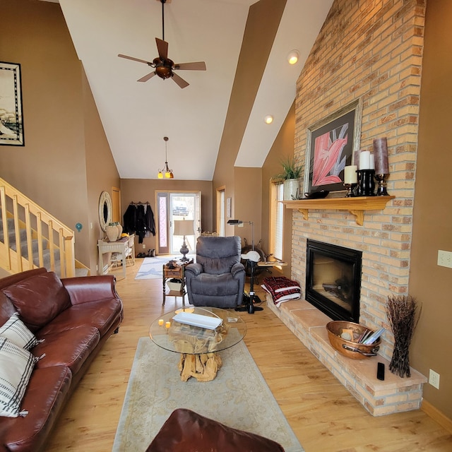 living room with ceiling fan, high vaulted ceiling, light hardwood / wood-style floors, and a brick fireplace