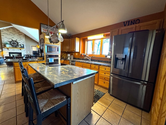 kitchen with lofted ceiling, a kitchen breakfast bar, a fireplace, appliances with stainless steel finishes, and a kitchen island