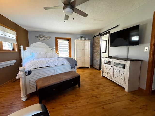 bedroom with a barn door, ceiling fan, wood-type flooring, and a textured ceiling