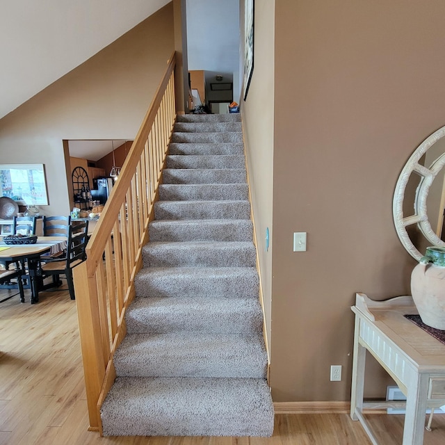 stairway with wood-type flooring, vaulted ceiling, and an inviting chandelier