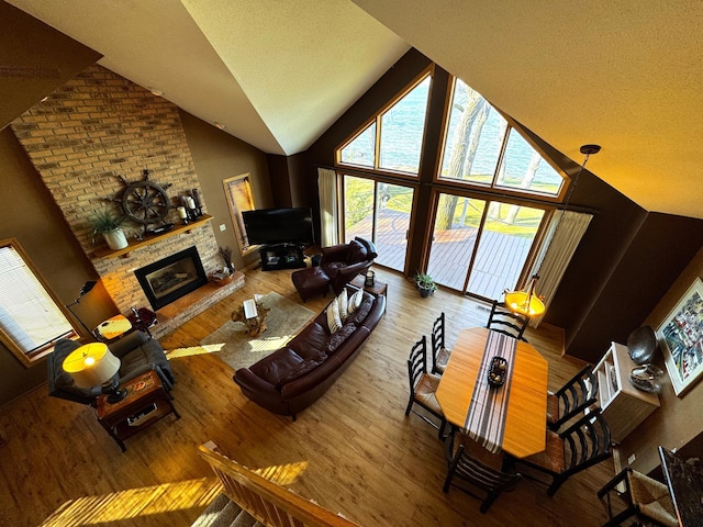 living room featuring wood-type flooring, high vaulted ceiling, and a brick fireplace