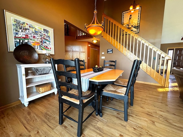 dining room featuring stairs, wood finished floors, a towering ceiling, and baseboards