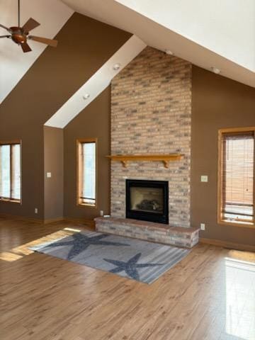 unfurnished living room with a ceiling fan, a brick fireplace, wood finished floors, high vaulted ceiling, and baseboards