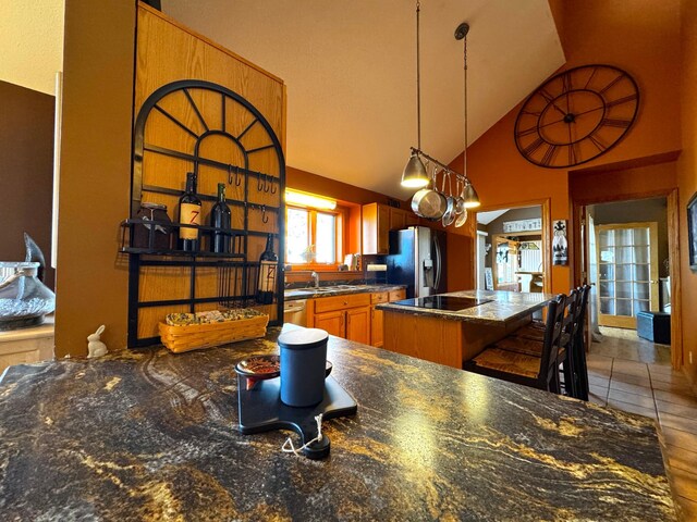 kitchen featuring high vaulted ceiling, a sink, a kitchen island, stainless steel refrigerator with ice dispenser, and dark countertops