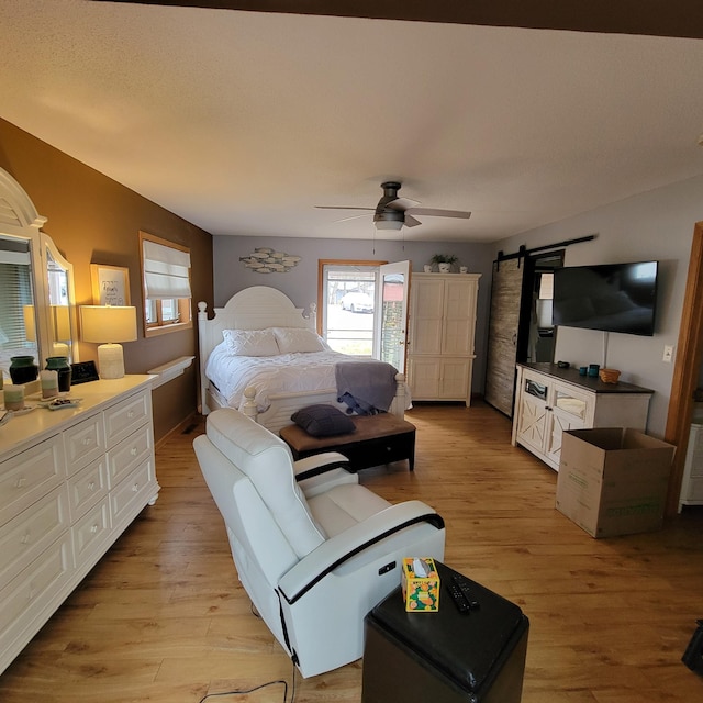 bedroom featuring a barn door, light wood-style flooring, and a ceiling fan