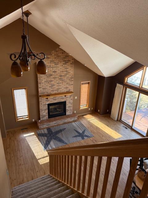 unfurnished living room featuring an inviting chandelier, a brick fireplace, a textured ceiling, wood finished floors, and high vaulted ceiling