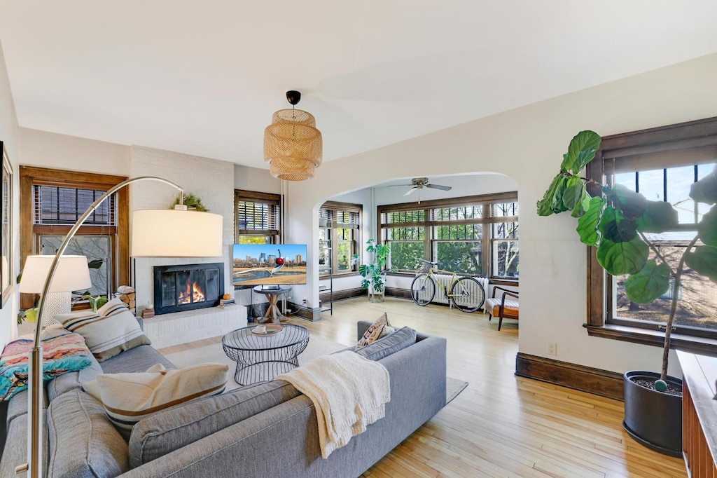 living room featuring ceiling fan, a large fireplace, and light hardwood / wood-style flooring