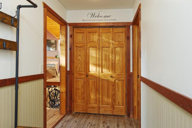 corridor with light hardwood / wood-style floors, a textured ceiling, and wooden walls