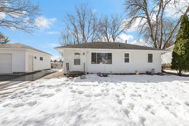 snow covered rear of property with an outdoor structure and a garage