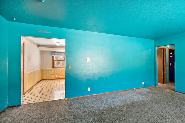 carpeted empty room with visible vents, wooden walls, a textured ceiling, and wainscoting