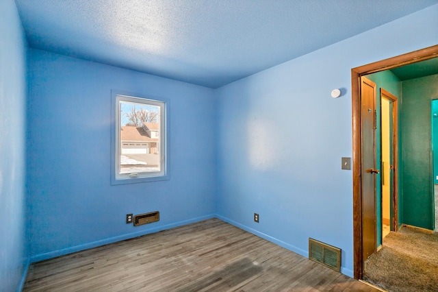 unfurnished room featuring visible vents, baseboards, a textured ceiling, and wood finished floors