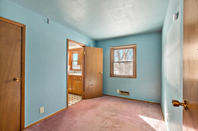 unfurnished bedroom featuring connected bathroom, baseboards, carpet, and a textured ceiling