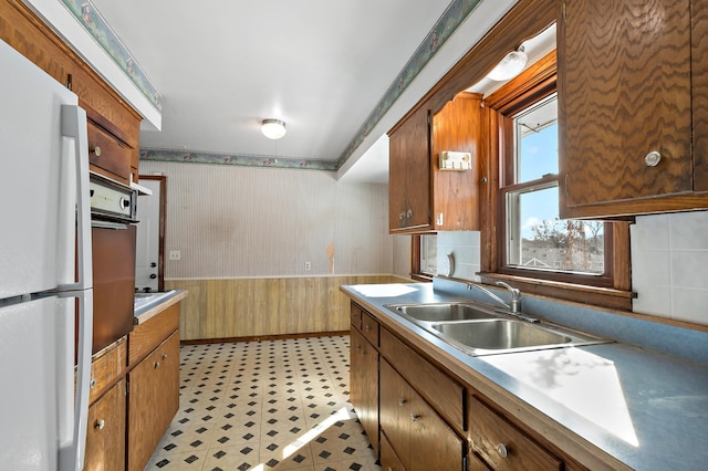 kitchen featuring light floors, wallpapered walls, freestanding refrigerator, a sink, and wainscoting