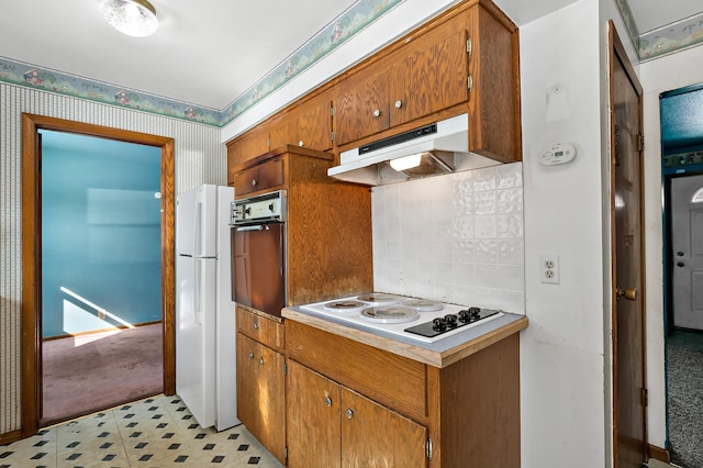 kitchen with under cabinet range hood, tasteful backsplash, white appliances, brown cabinetry, and wallpapered walls