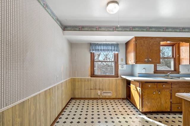 kitchen with wainscoting, wallpapered walls, light floors, and a sink