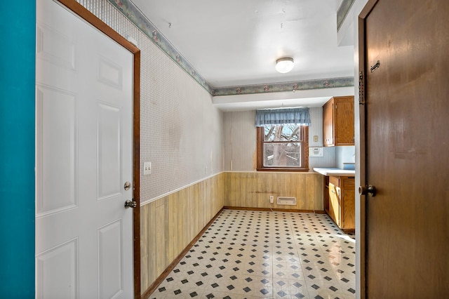 interior space featuring light floors, a wainscoted wall, wallpapered walls, light countertops, and wood walls