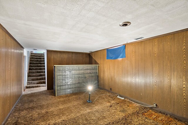 interior space featuring visible vents, carpet floors, stairs, wood walls, and a textured ceiling