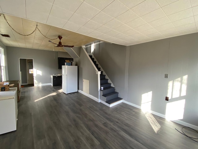 unfurnished living room with stairway, baseboards, a ceiling fan, and dark wood finished floors
