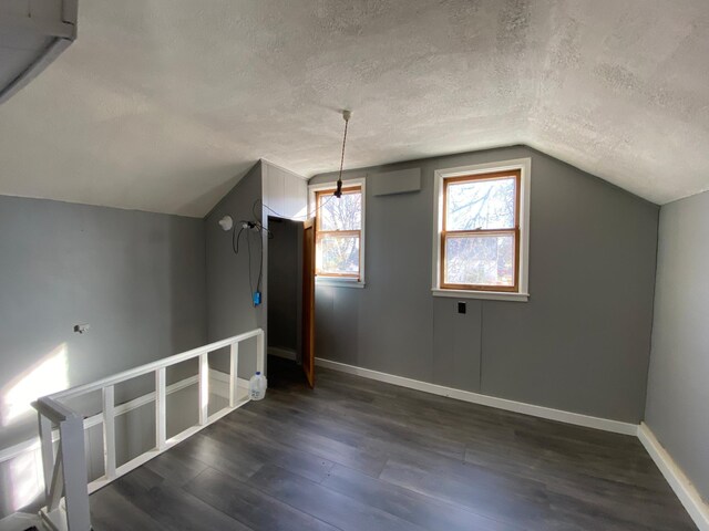 bonus room with a textured ceiling, vaulted ceiling, baseboards, and dark wood-type flooring