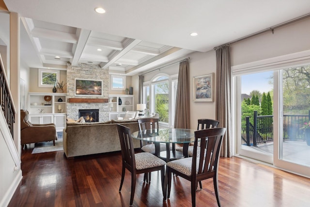 dining space featuring coffered ceiling, beamed ceiling, dark wood-type flooring, a stone fireplace, and recessed lighting