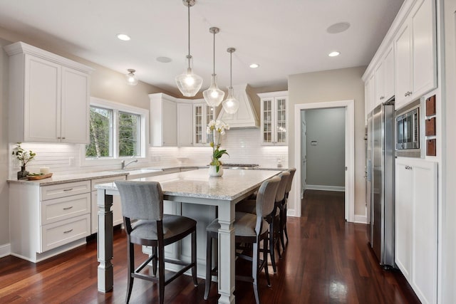 kitchen with white cabinets, glass insert cabinets, dark wood-style flooring, a center island, and pendant lighting