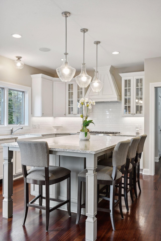 kitchen with a center island, pendant lighting, glass insert cabinets, white cabinets, and premium range hood